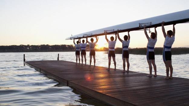 Rowing team holding up boat at sunrise